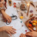 Hands arranging astrology charts with candles and crystals on a table for a spiritual ritual.